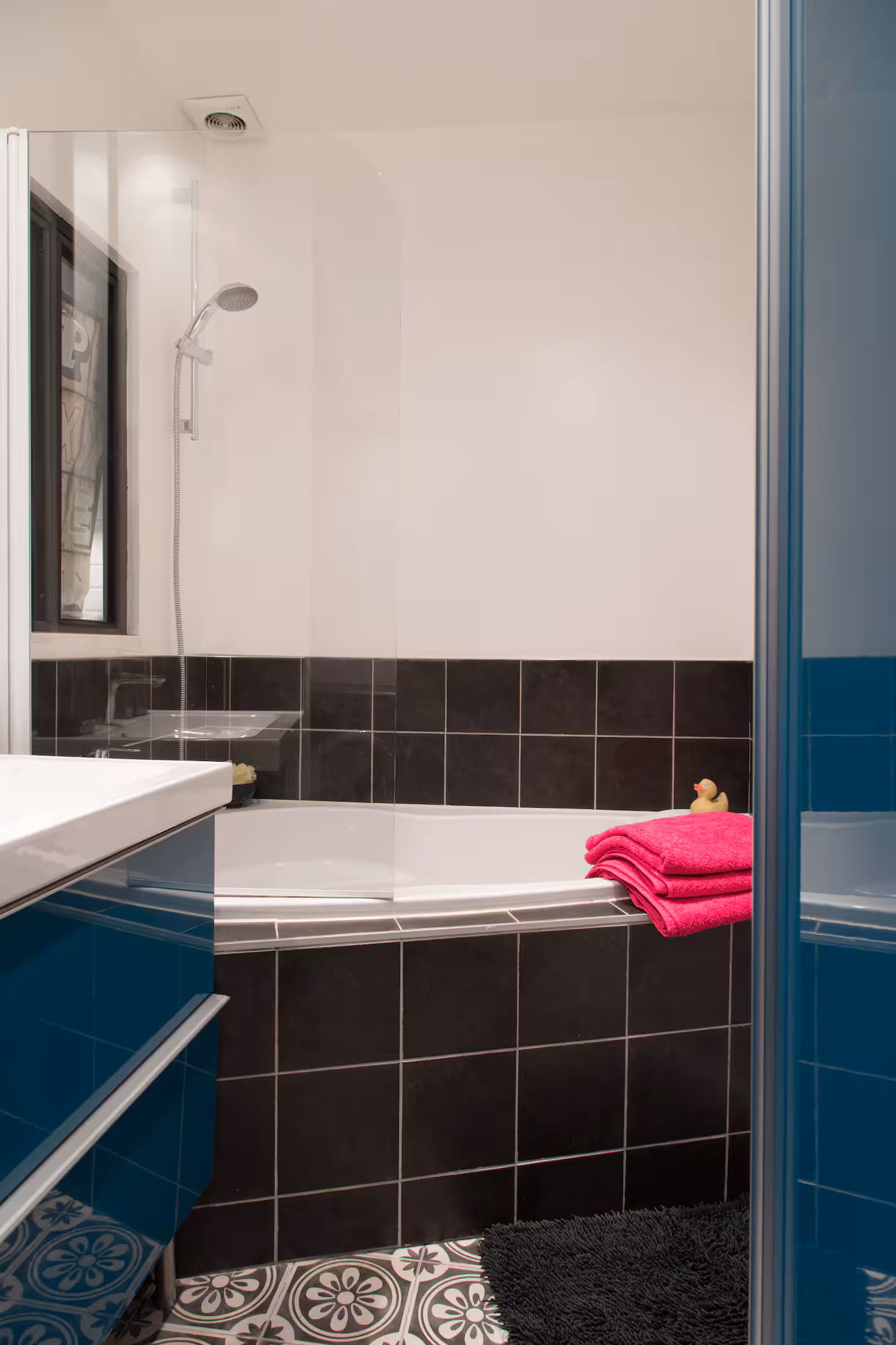 Salle de bain carrelée de noir avec baignoire, appartement géré par Le Double des Clés