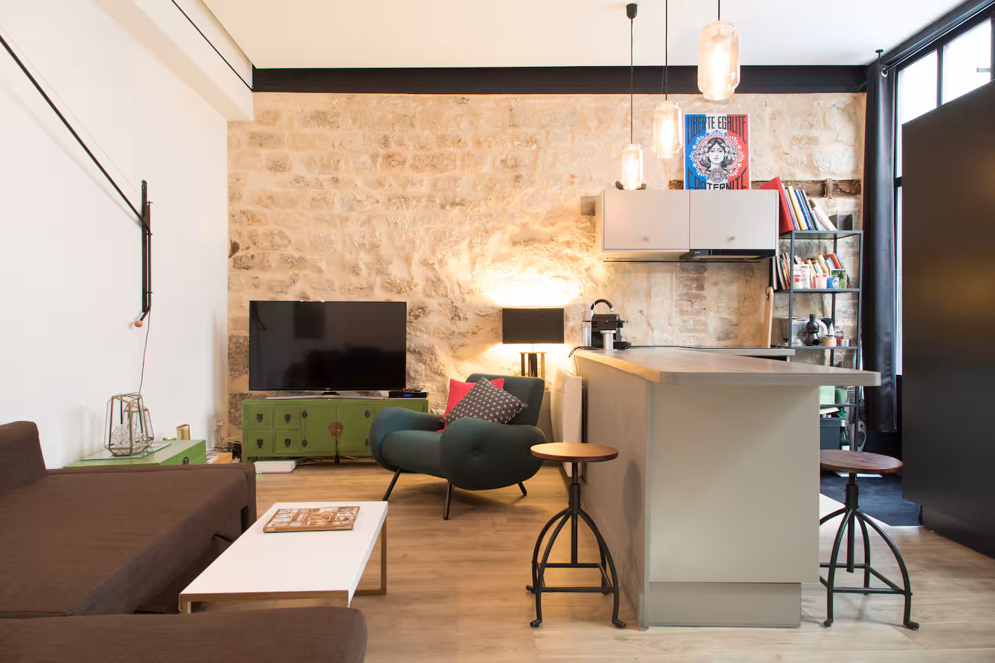 Séjour avec cuisine ouverte et mur de pierre apparente, appartement géré par Le Double des Clés